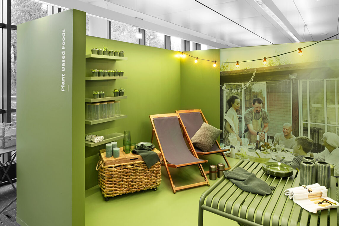 Symrise Messestand von einem grünen Raum mit Liegestühlen und einem Tisch und Picknickkorb
